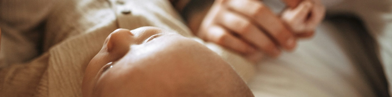 Close-up of a baby lying against a parent's chest, with the parent gently holding the baby's tiny hand.