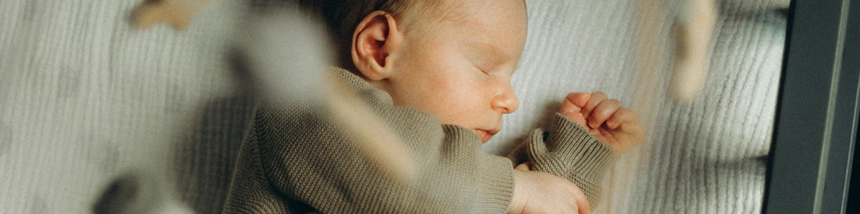 A sleeping newborn baby lies on a textured blanket in a nursery.